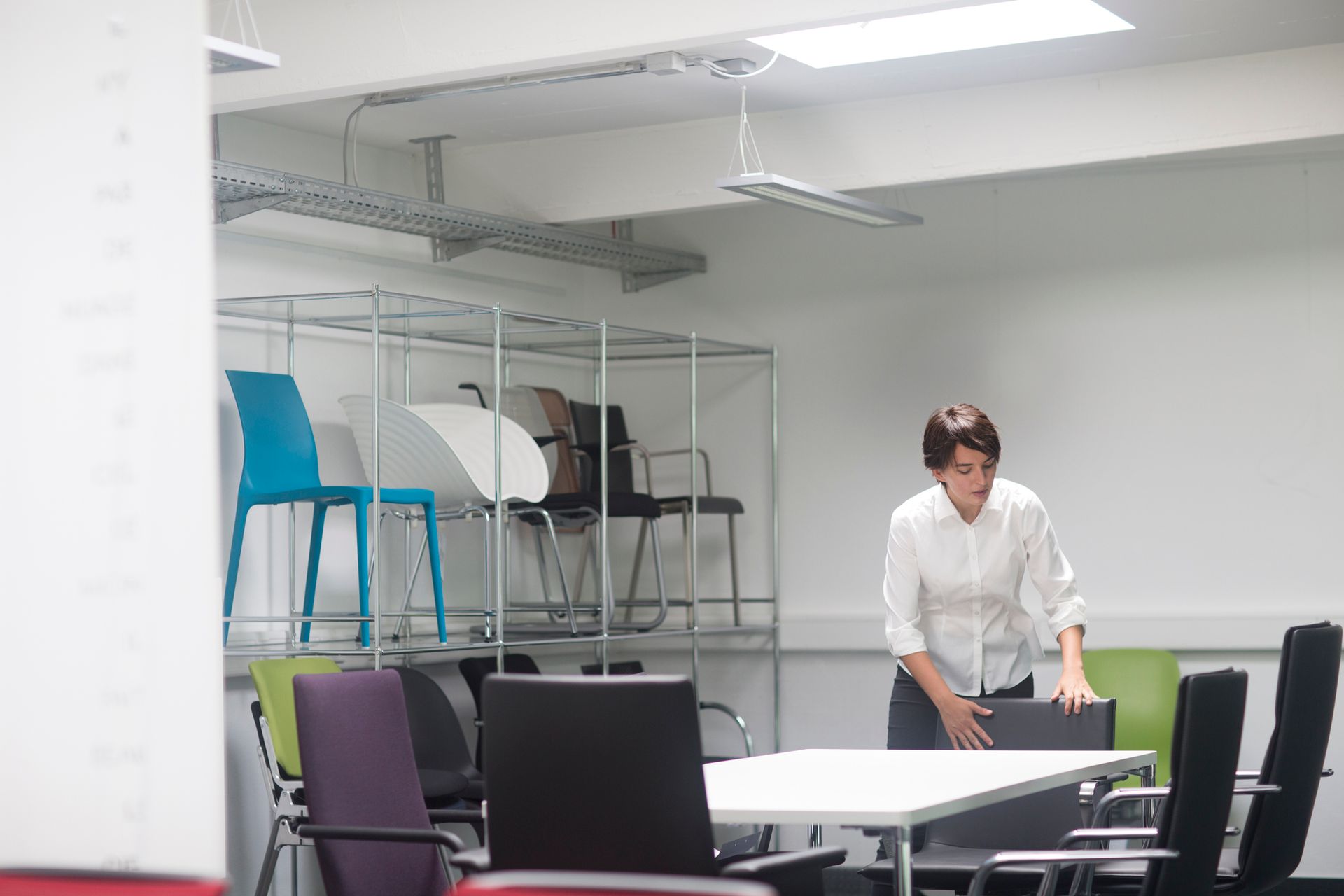 Young female sales manager organizing chairs in office furniture store.