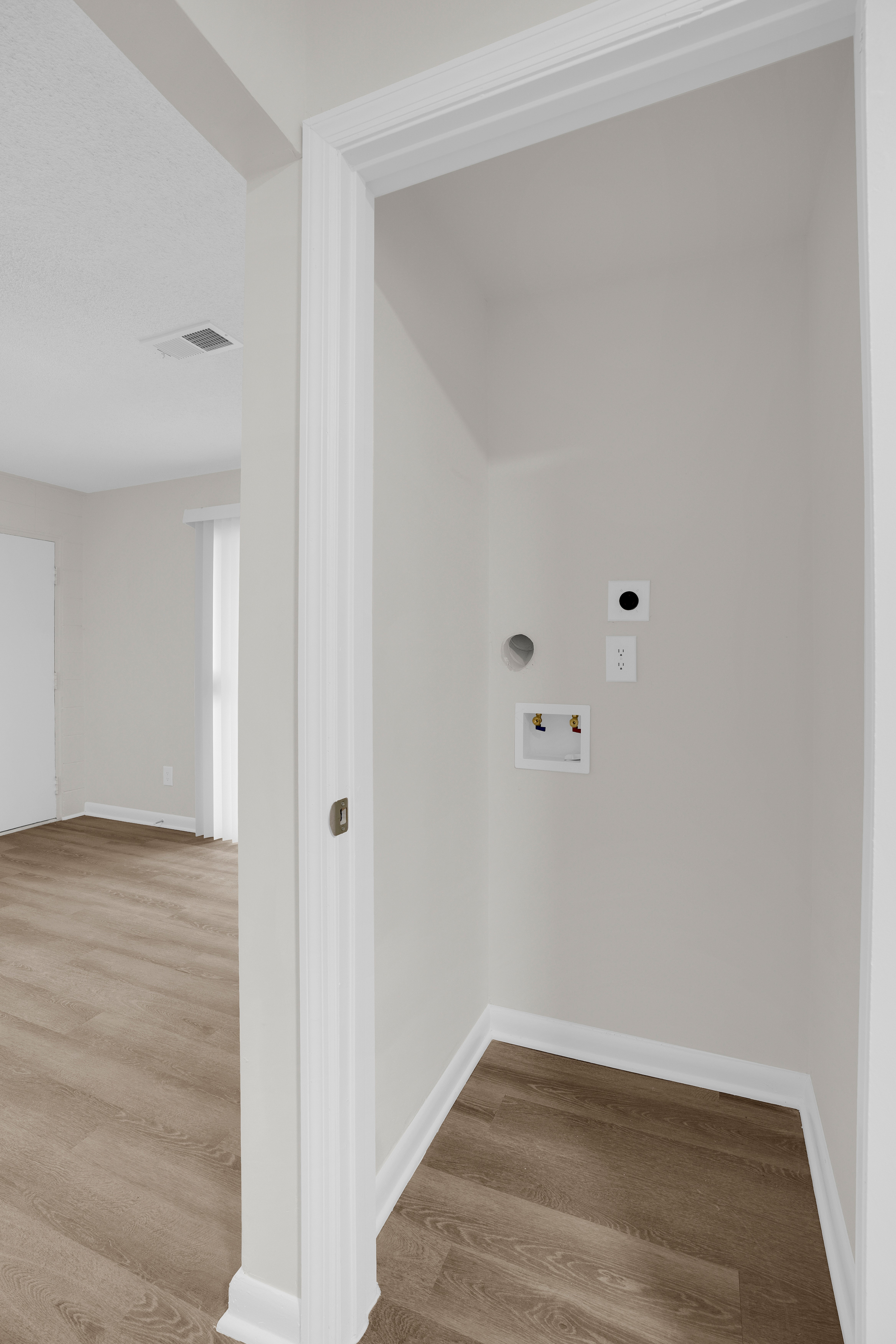An interior view of a laundry closet featuring a washer hookup and dryer vent, adjacent to a carpeted room.