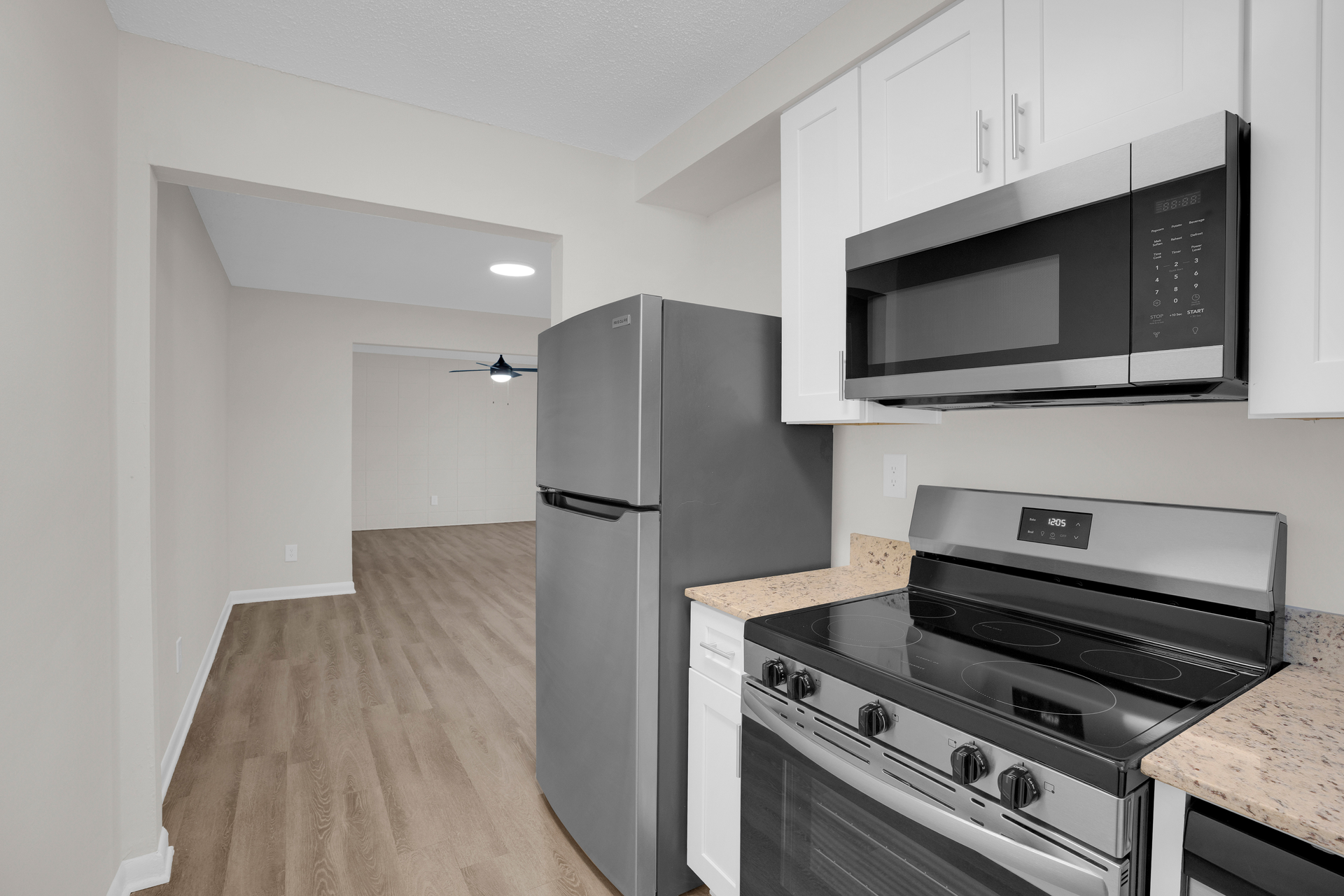 A modern kitchen with stainless steel appliances, white cabinets, and wood-look flooring leading into an open room.
