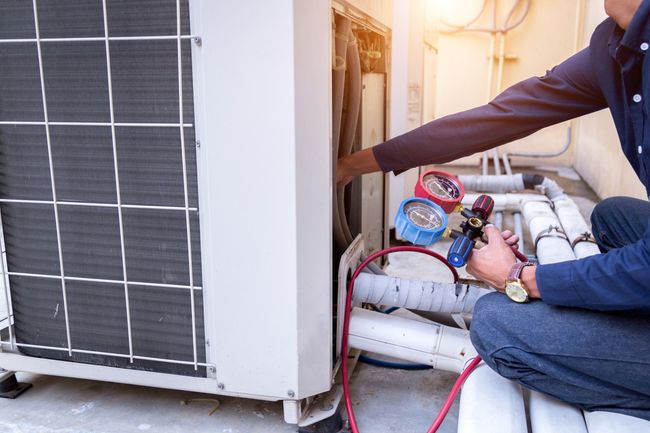 Technician using gauges to service an outdoor air conditioner unit with red hoses attached