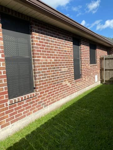 Brick wall of a building with three windows, black screens, and green grass. Blue sky in background.