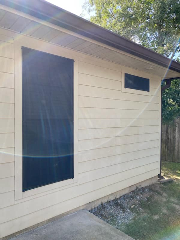 Beige building with large black solar panel and small black window.