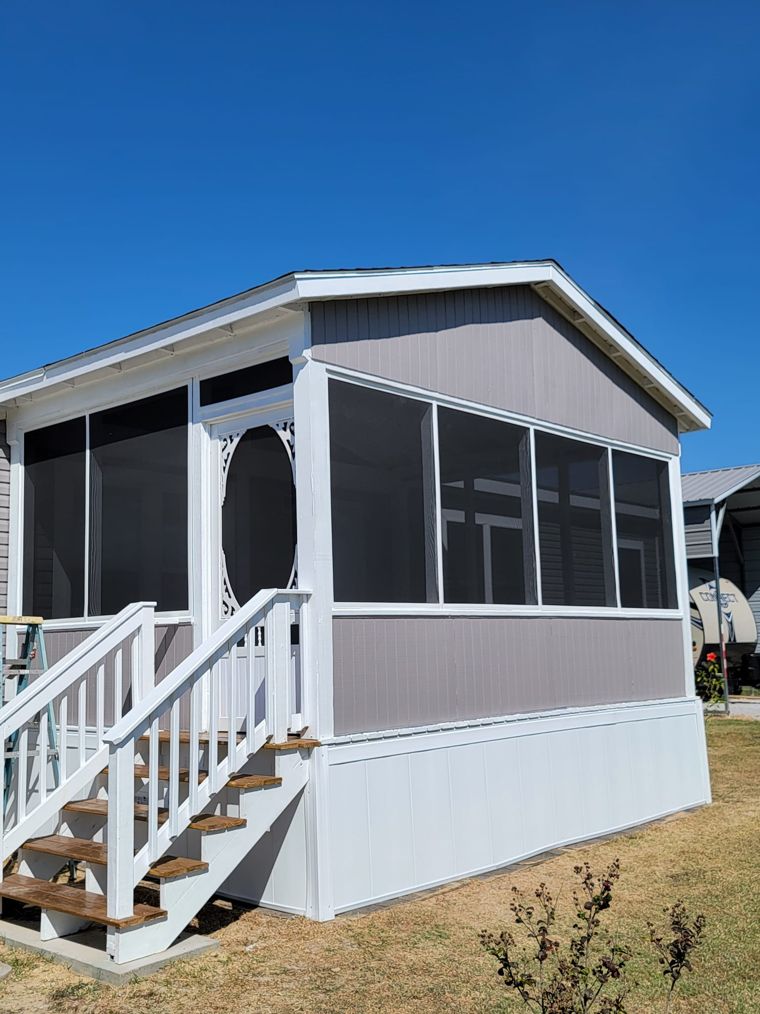 Screened porch with white steps and railing; gray siding against a blue sky.