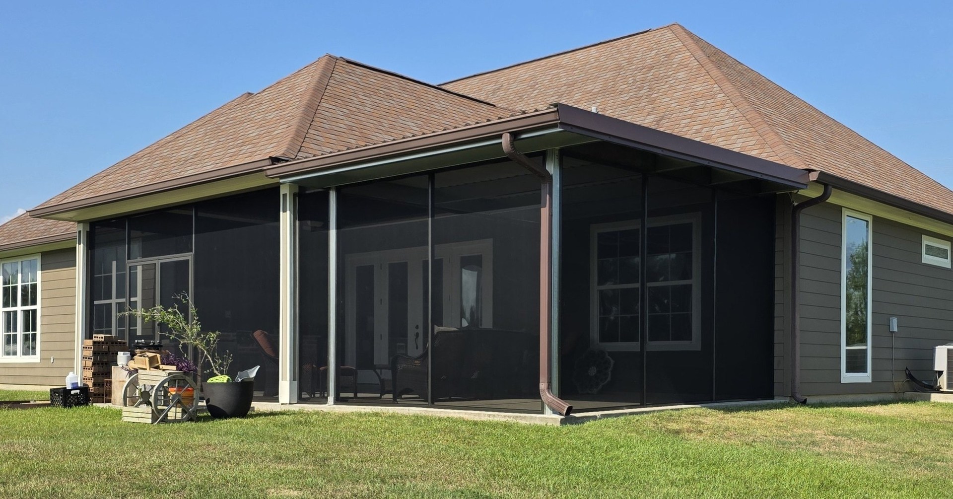 Screened porch attached to a house with brown roof and green lawn.