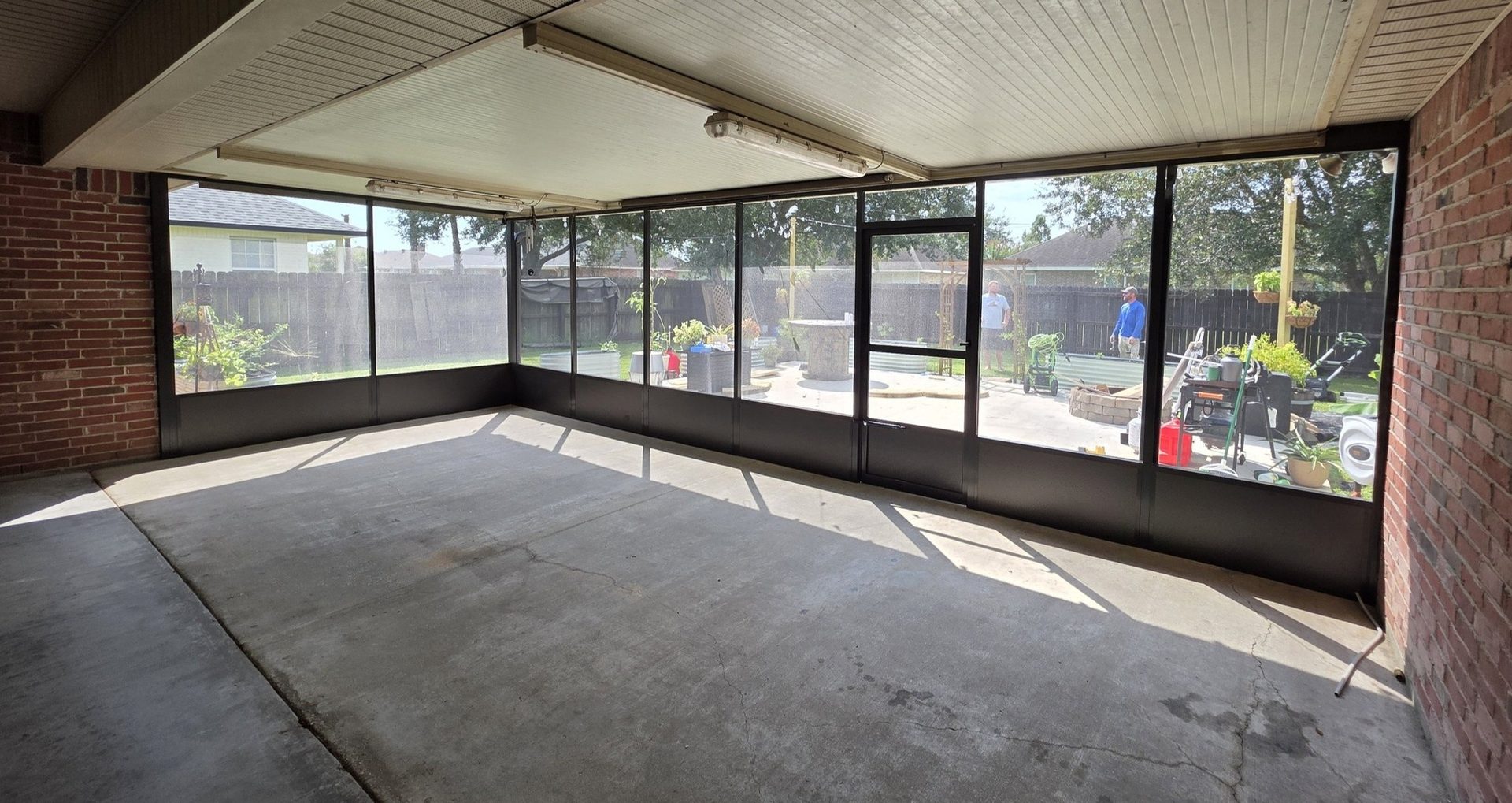 Enclosed patio with concrete floor, screened walls, and a door, attached to a brick building.