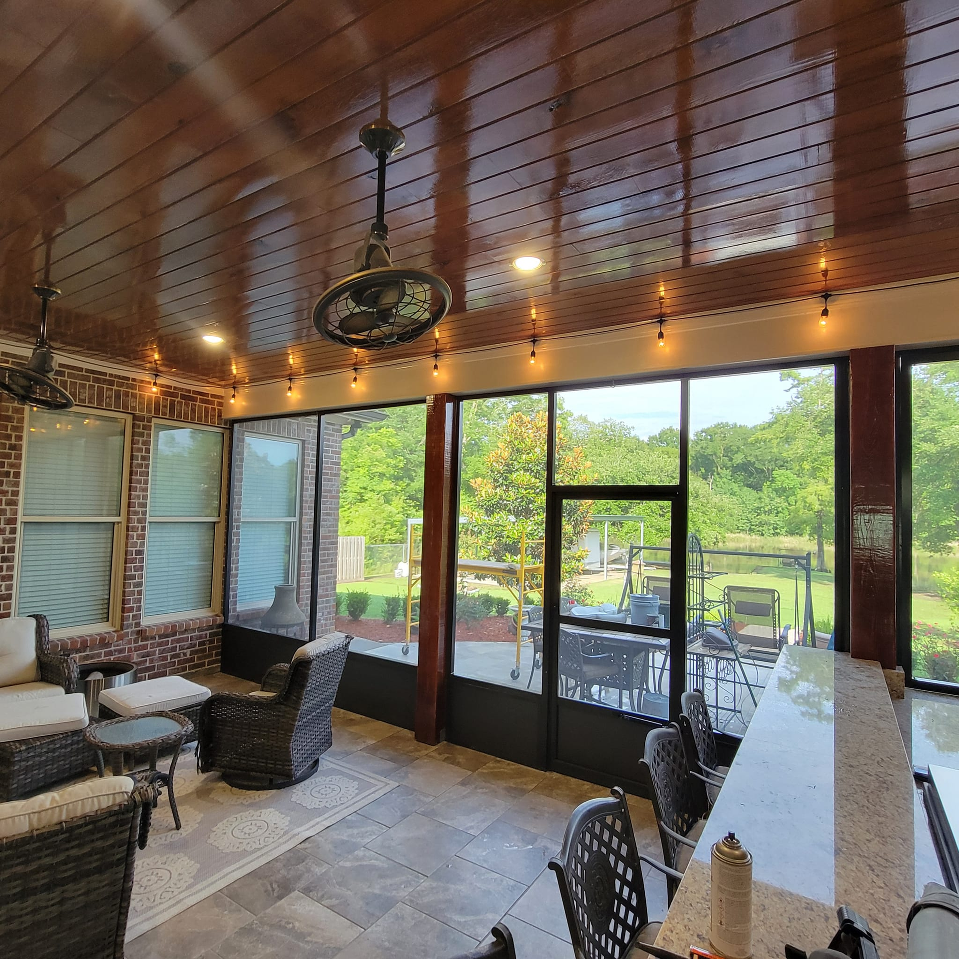Screened-in porch with seating, bar, and outdoor view. Ceiling fan and string lights illuminate the space.