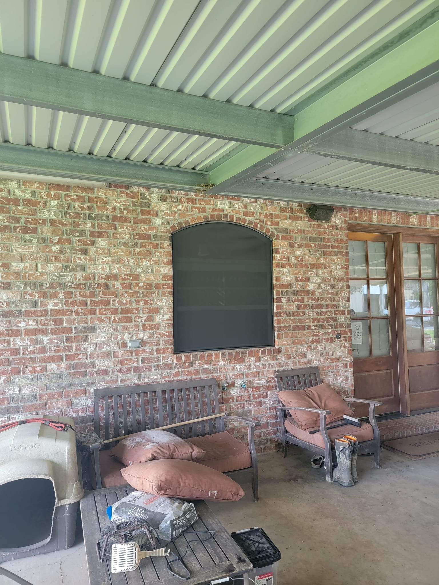 Patio with brick wall, seating, and a screened window. Covered by a corrugated metal roof.