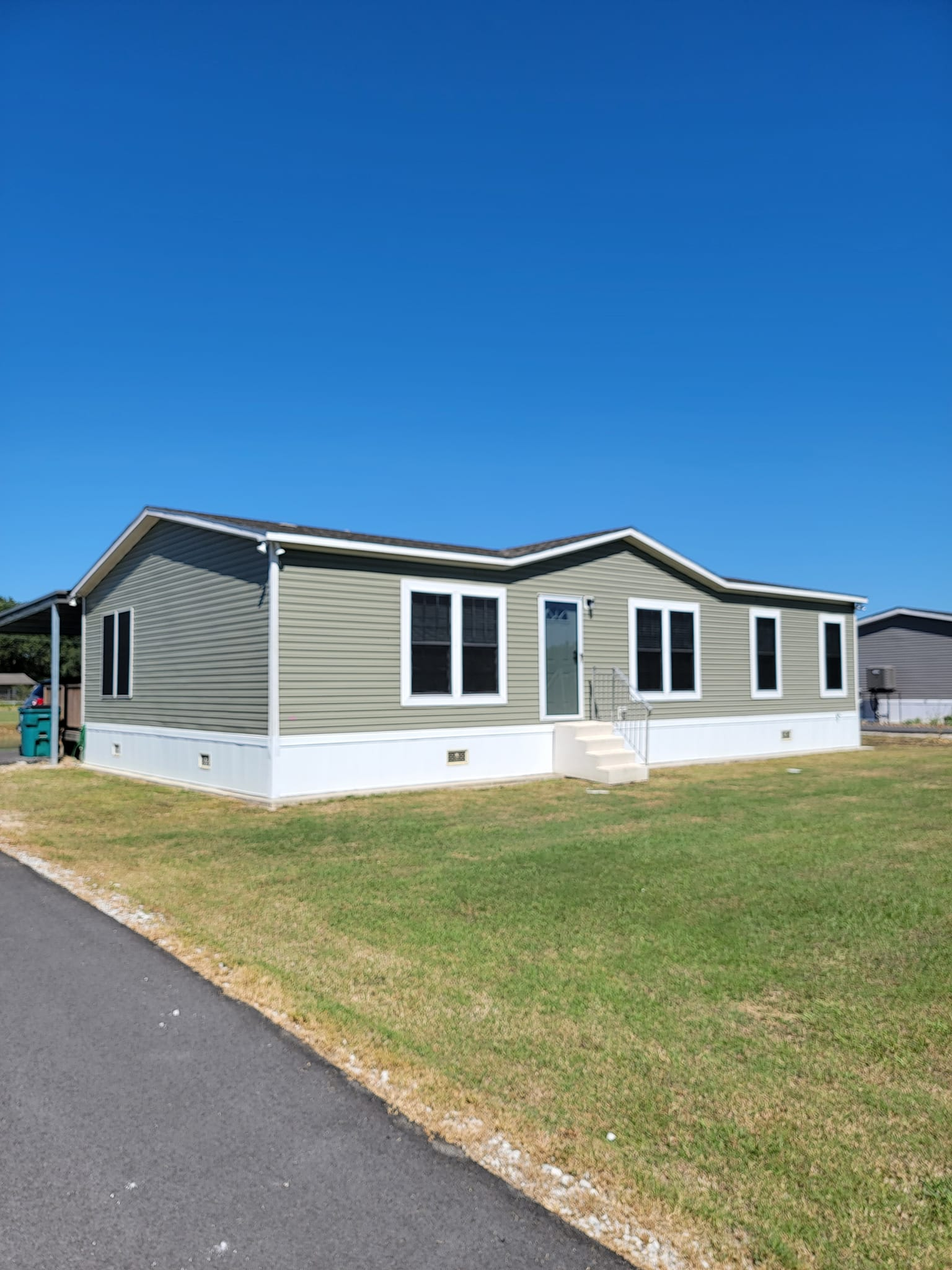 Green mobile home with white trim and a blue sky.
