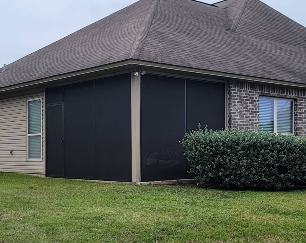 Black outdoor sun shades attached to a brick house. Green grass and bush in the foreground.