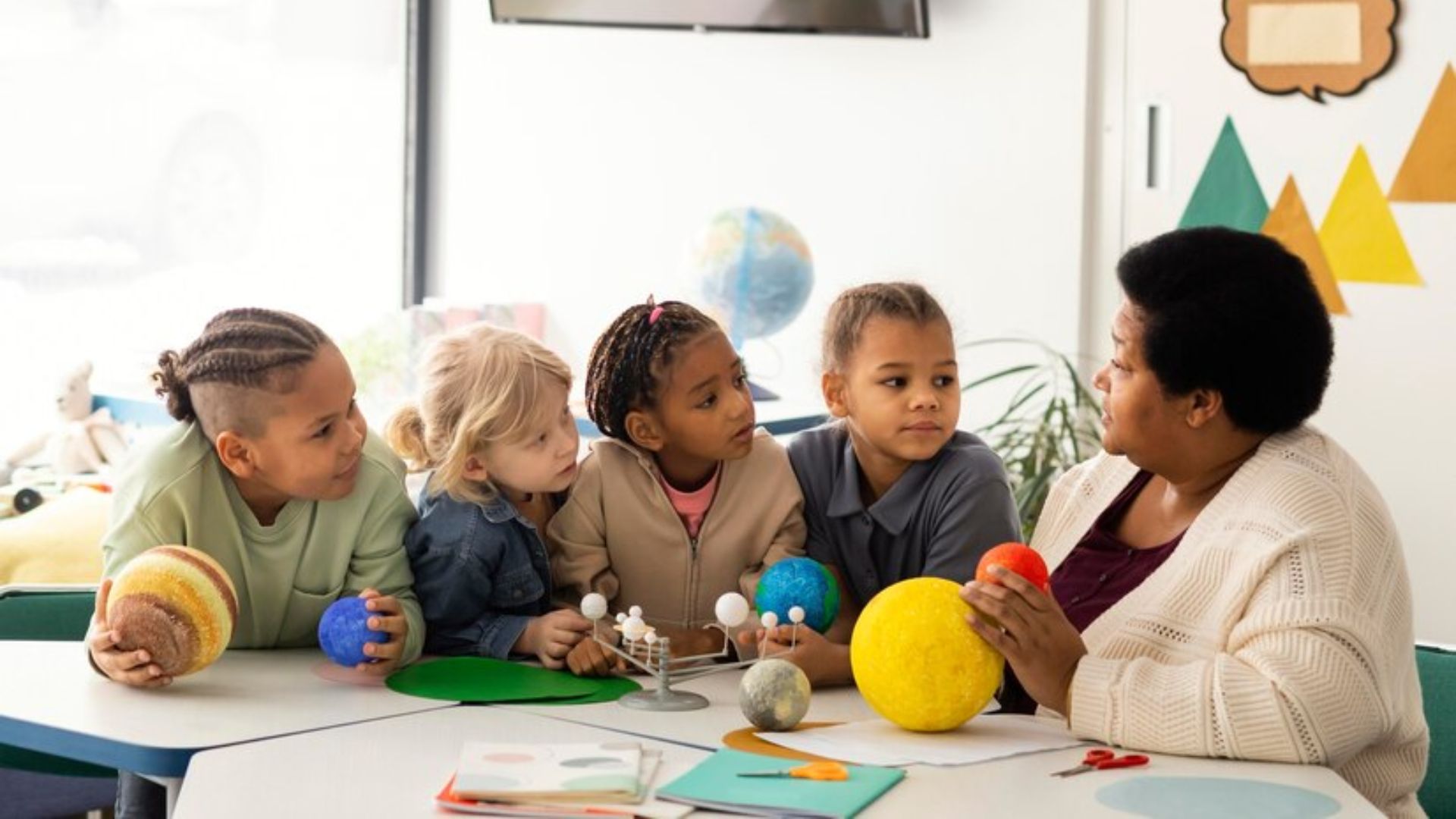 A group of children are sitting around a table with a teacher.
