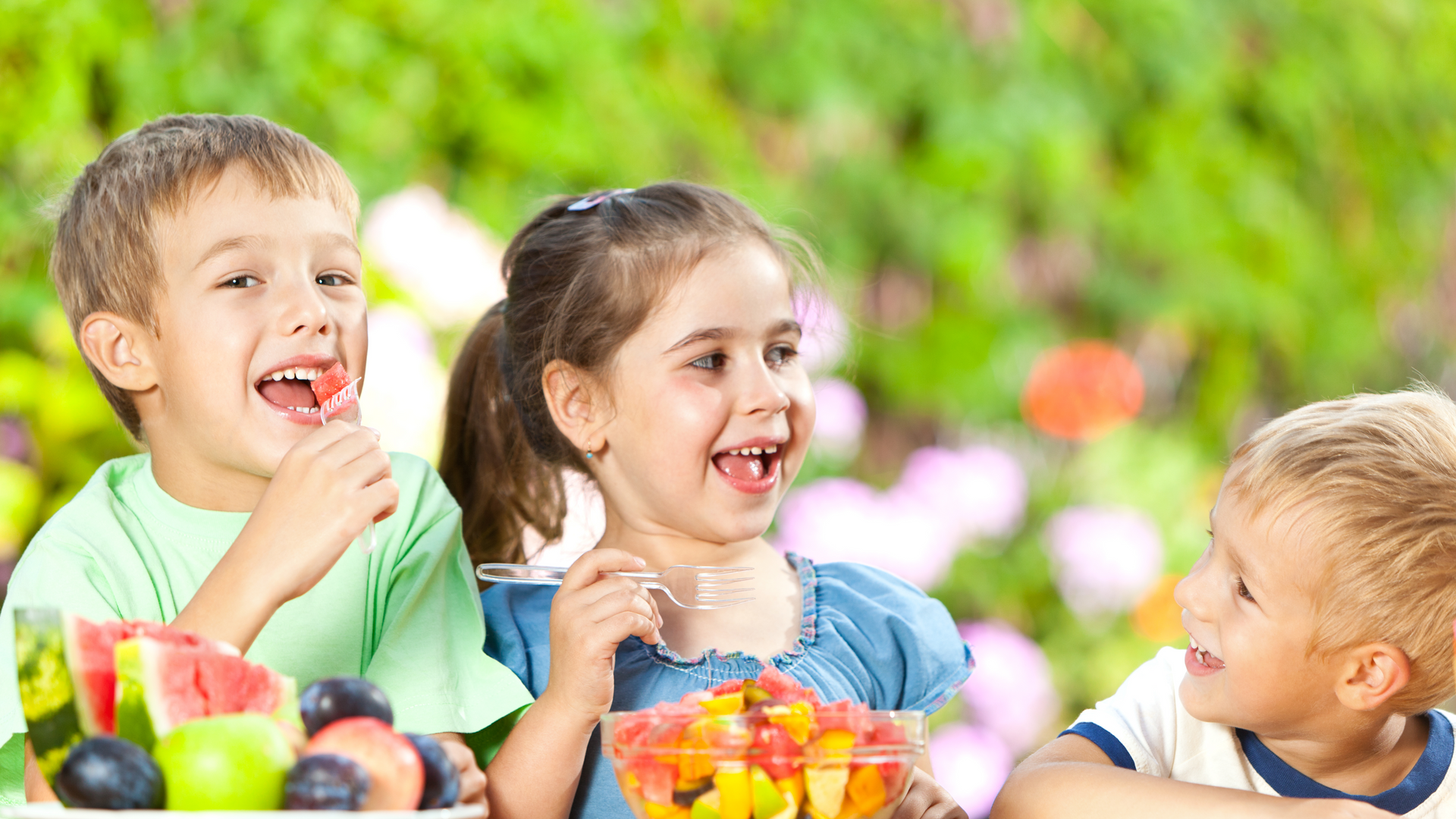 A group of children are sitting at a table eating fruit.
