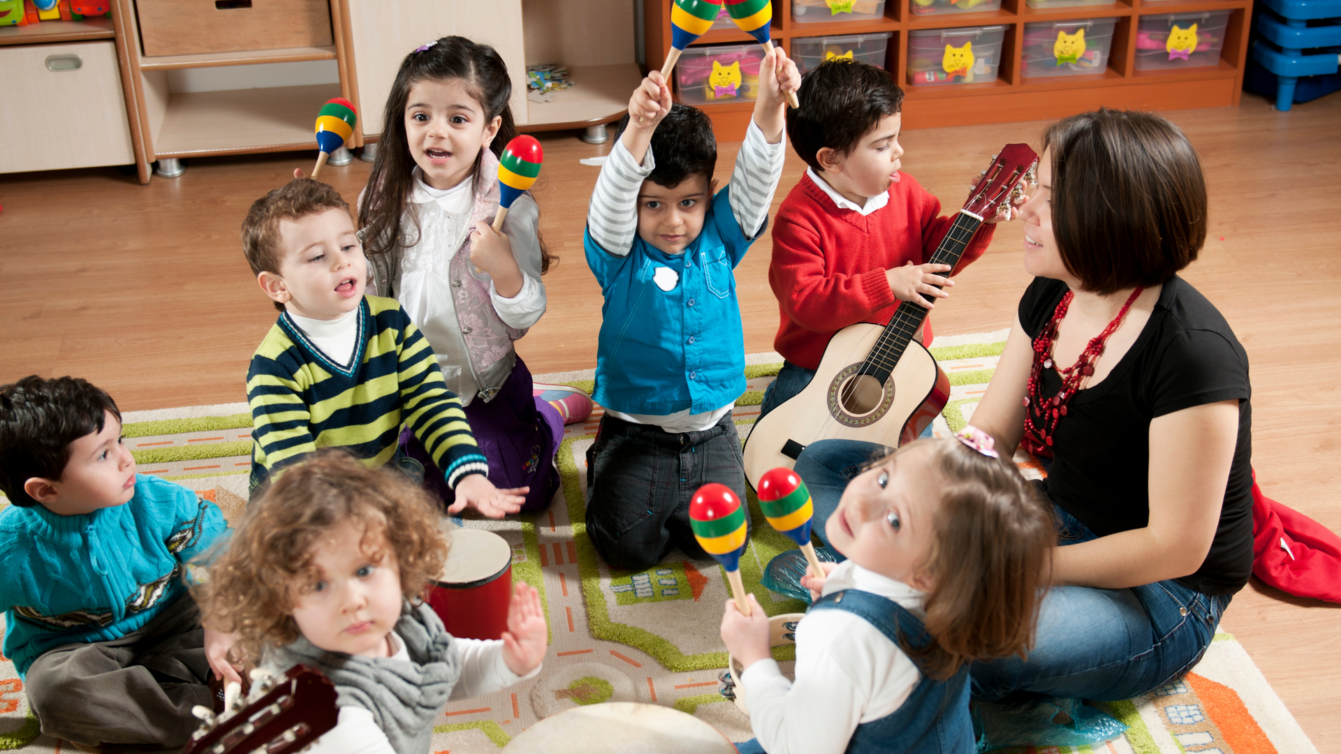 A group of children are sitting on the floor playing musical instruments.