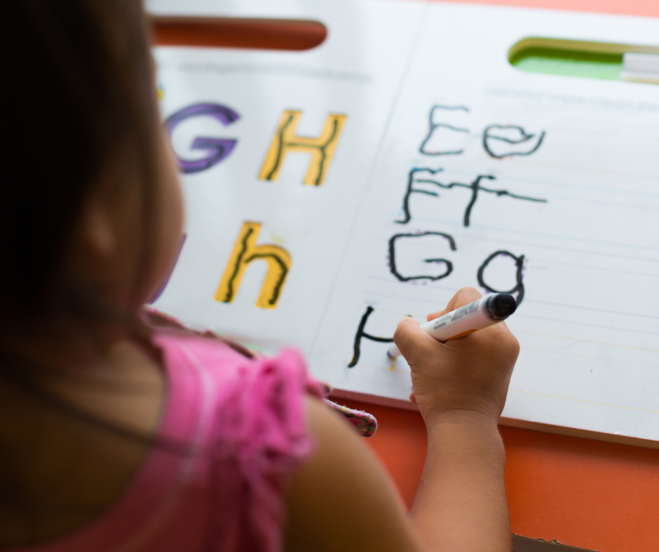 A little girl is writing on a piece of paper with a marker.