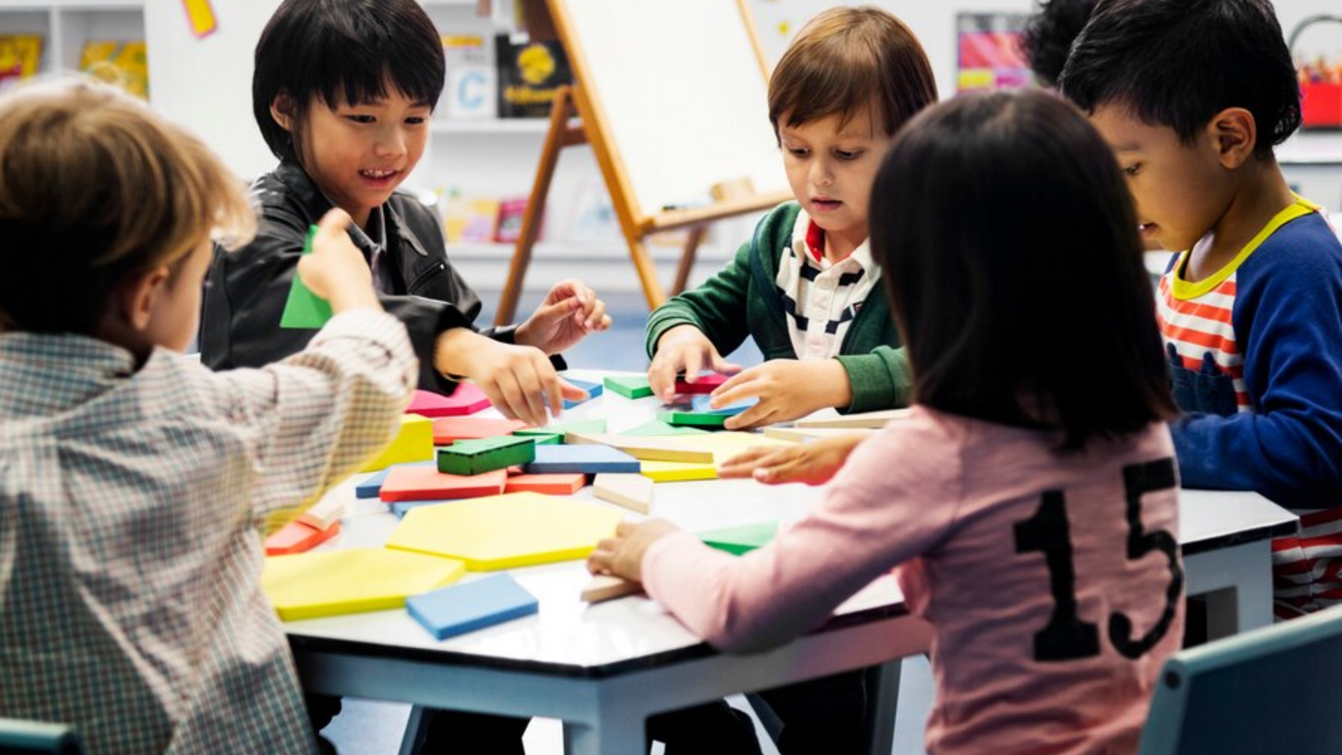 A group of children are sitting around a table playing with blocks.