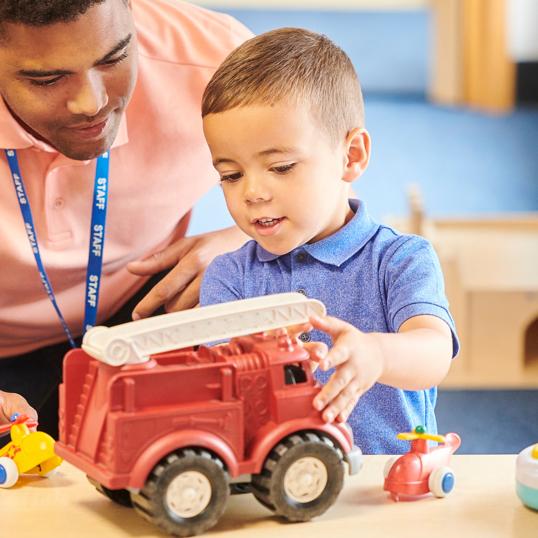 A little boy is playing with a red toy fire truck