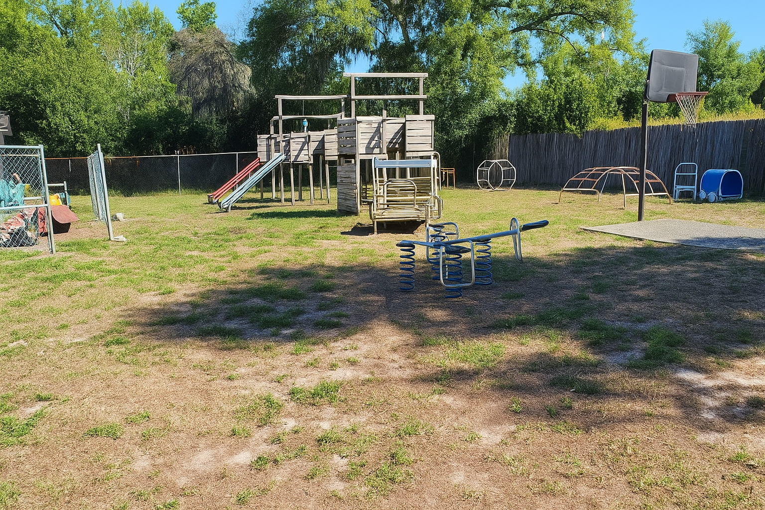Playground with wooden structures, slides, and a basketball hoop on a sunny day.