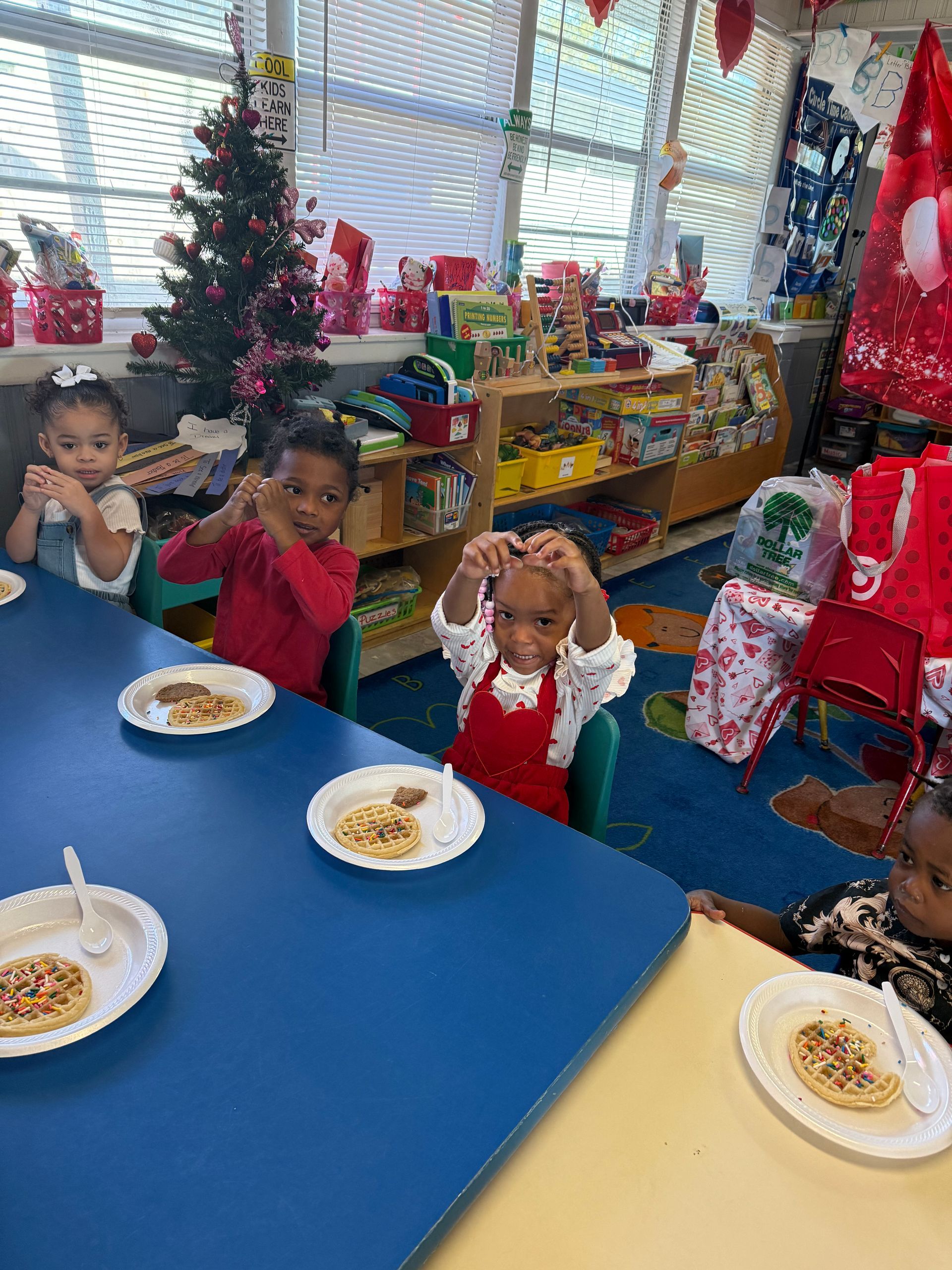 Children at a table with waffles, one making a heart with hands. Christmas decorations are in the room.