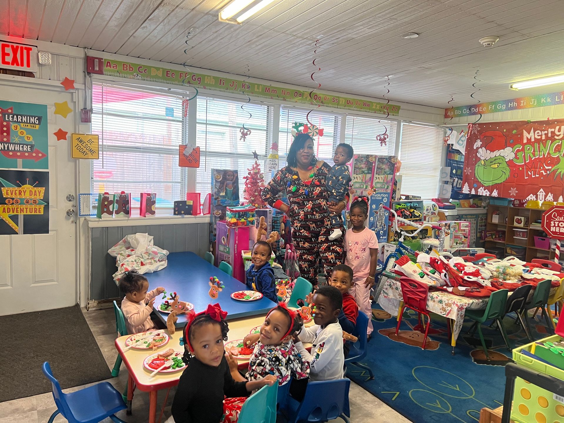 Children and an adult in pajamas at a holiday party in a decorated classroom.