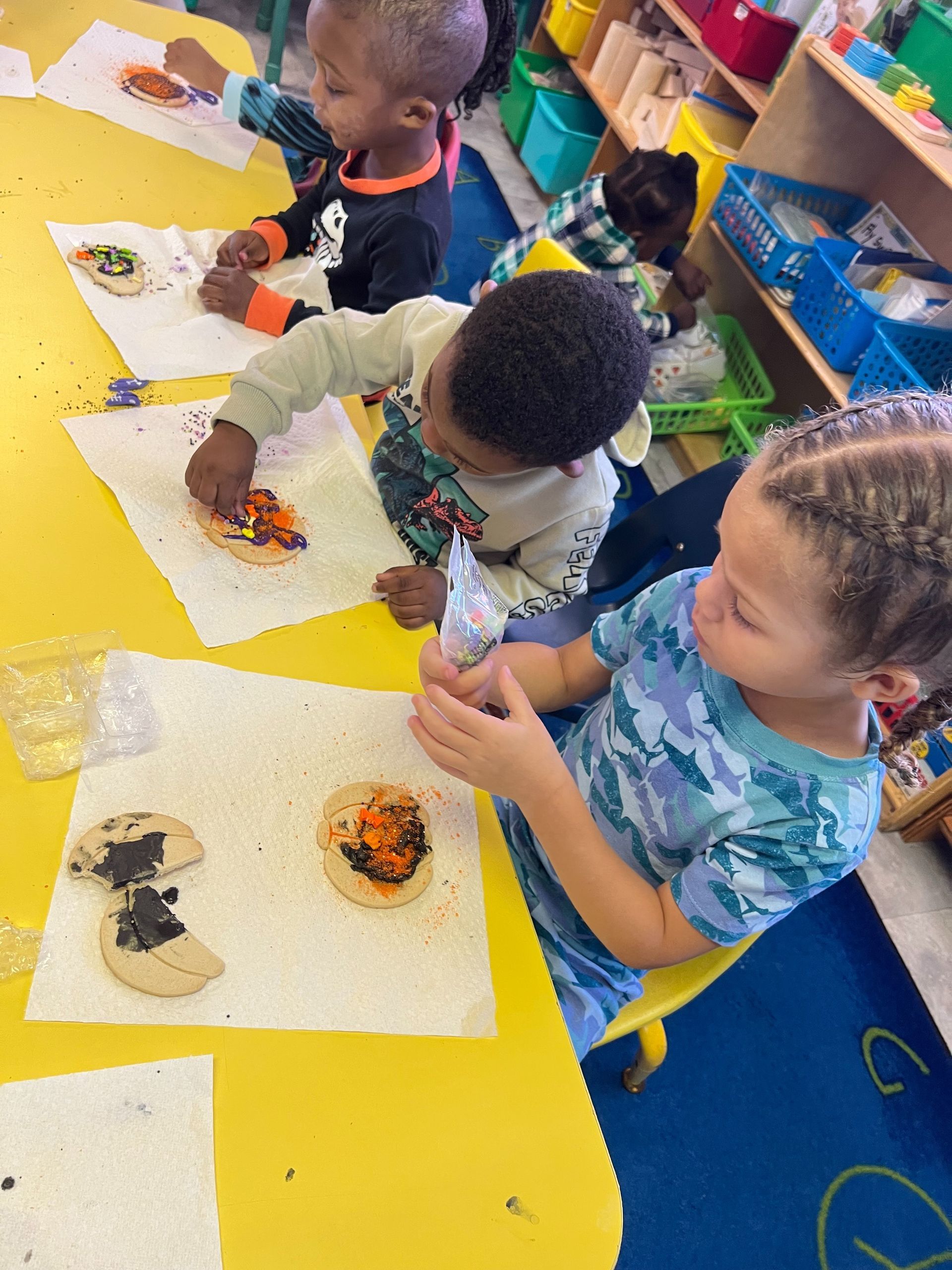 Children decorating cookies at a table, using frosting and sprinkles.