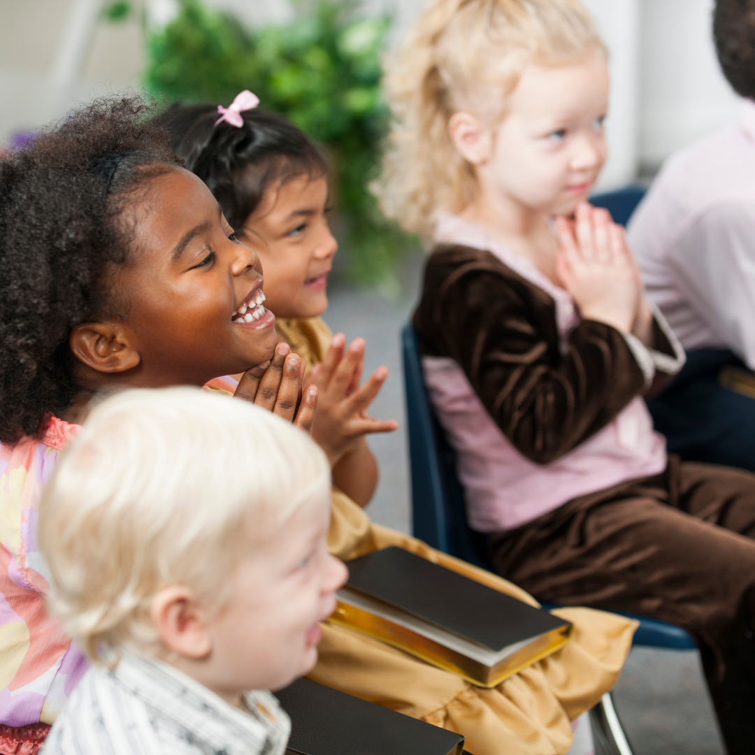 A group of children are sitting in chairs with a bible in their lap