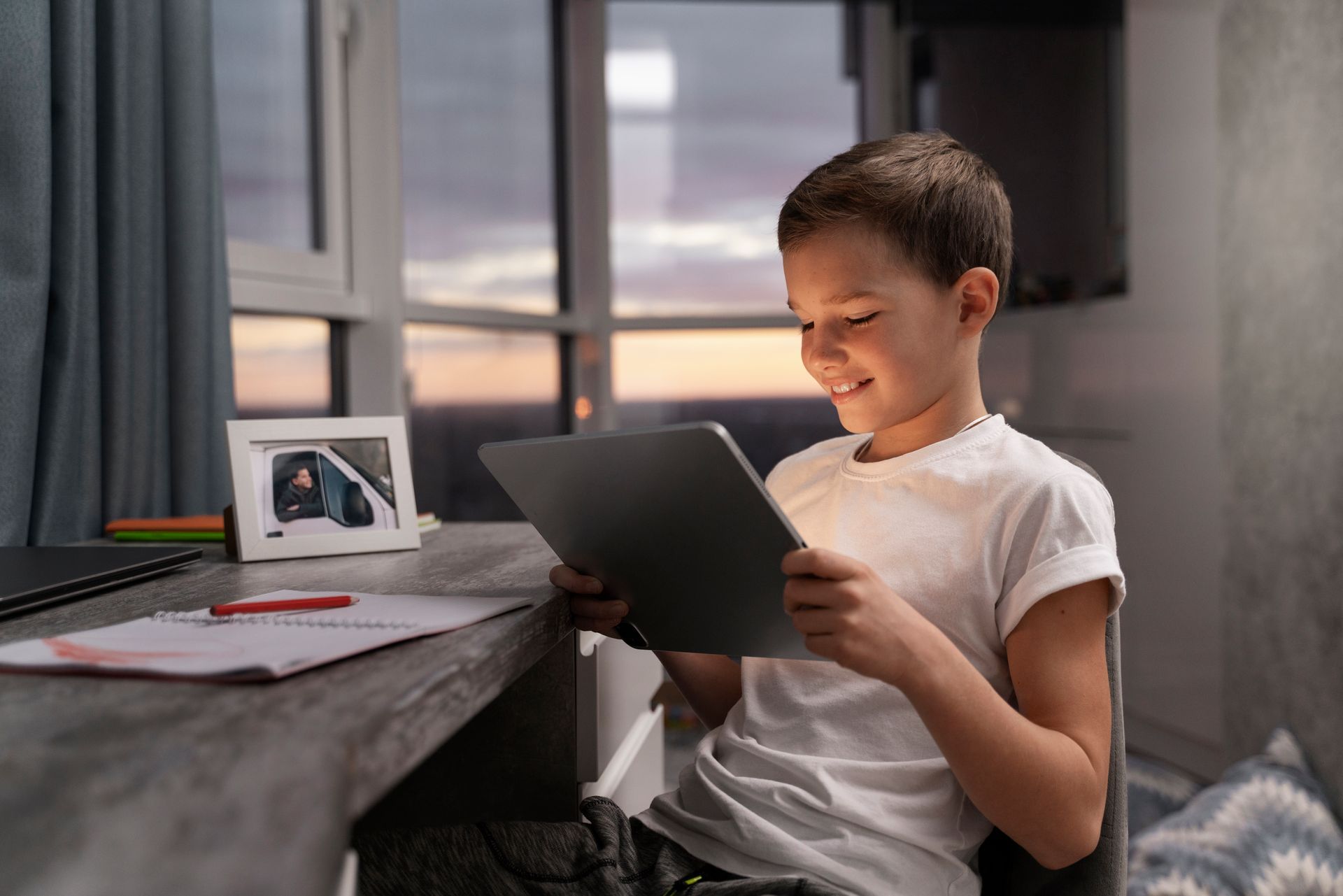 A young boy is sitting at a desk using a tablet computer.