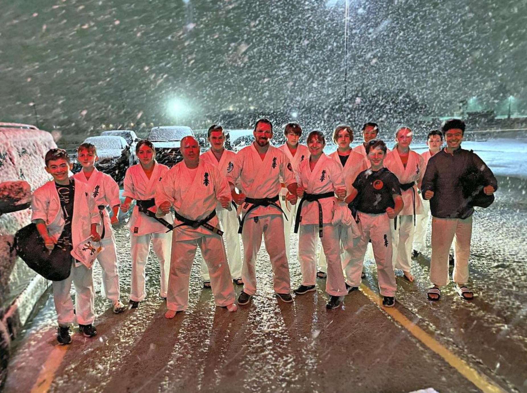 A group of people are standing in a parking lot in the snow.
