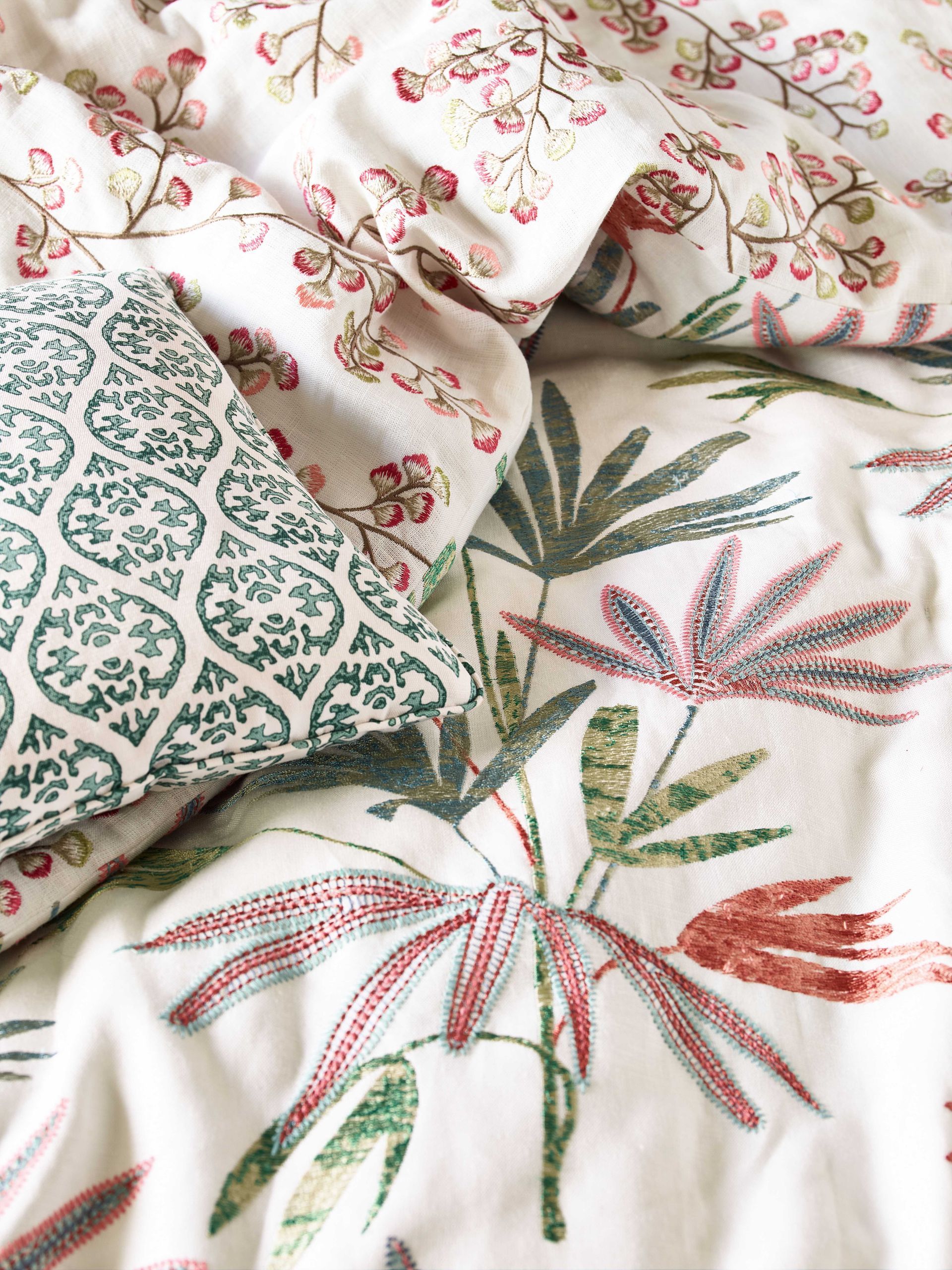 Bettwäsche mit Blumen- und Blättermuster; Kissen mit grünem geometrischem Muster.