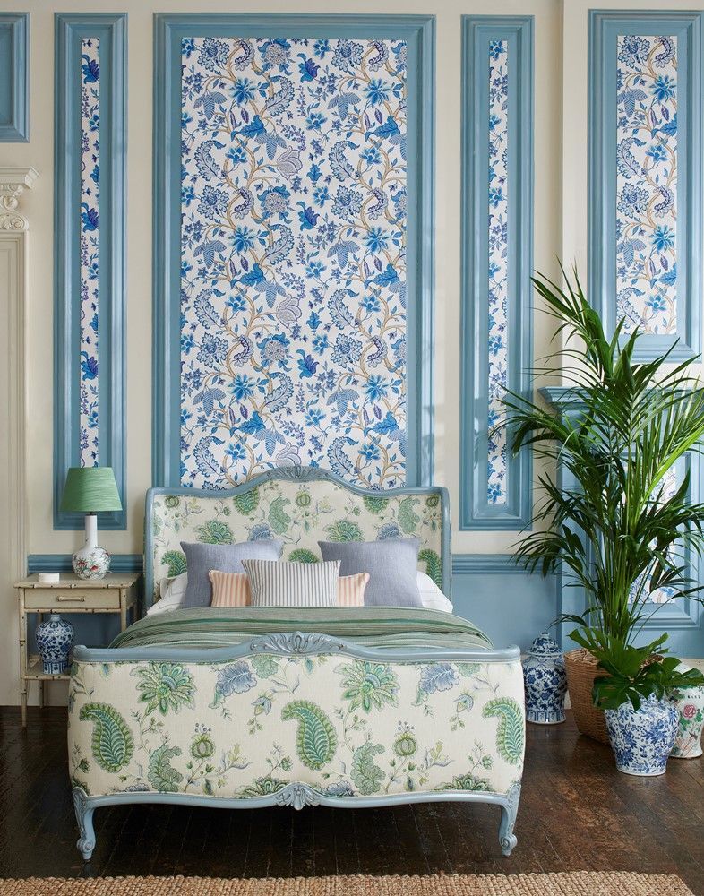 Schlafzimmer mit blau gemusterter Tapete und Zierleisten, einem mit Paisley-Muster bezogenen Bett und Topfpflanzen.