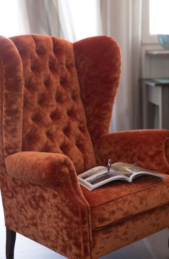 Ein orangefarbener, samtbezogener Sessel mit einem aufgeschlagenen Buch.