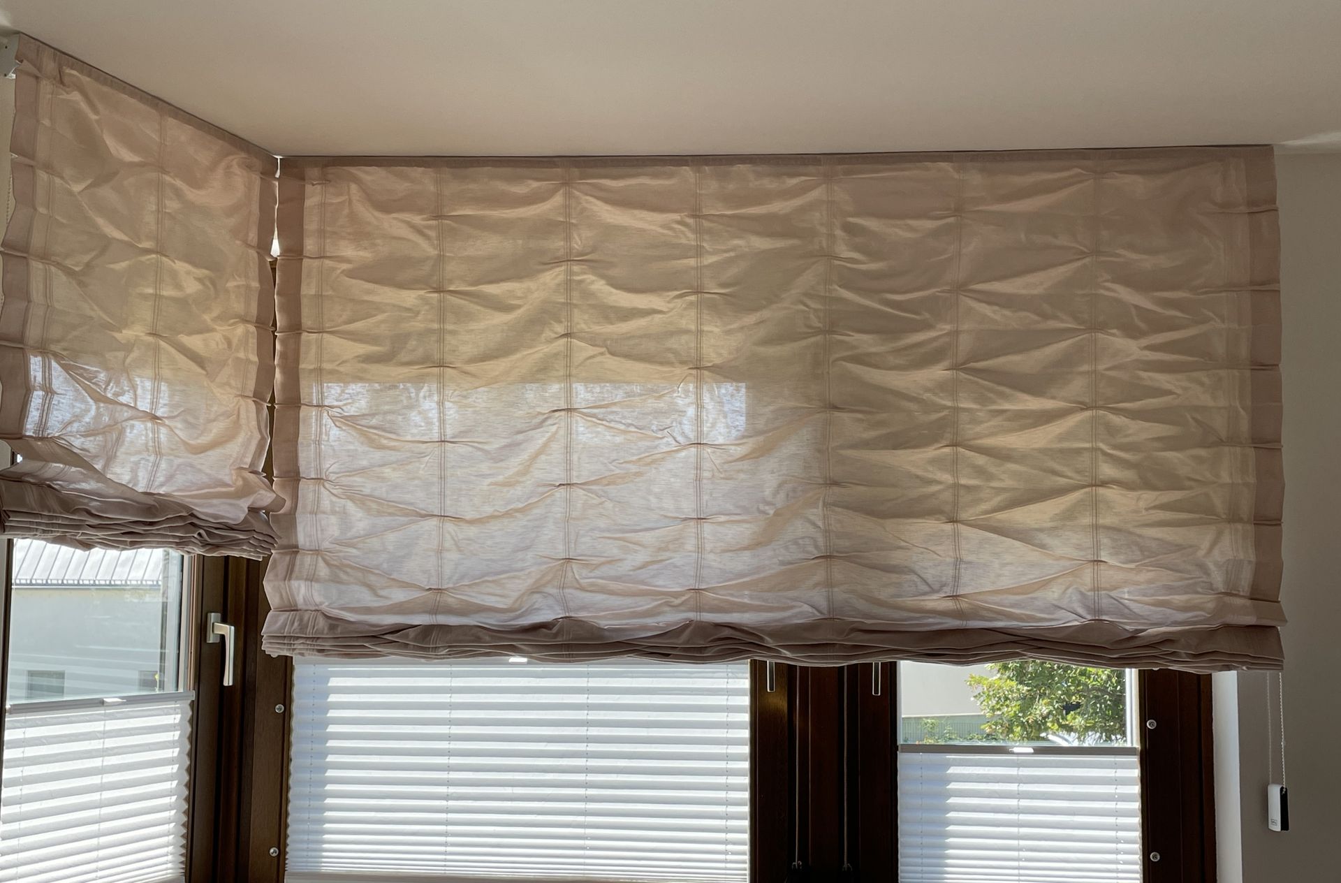 Beigefarbene römische Rollos, die die Fenster bedecken, teilweise hochgezogen