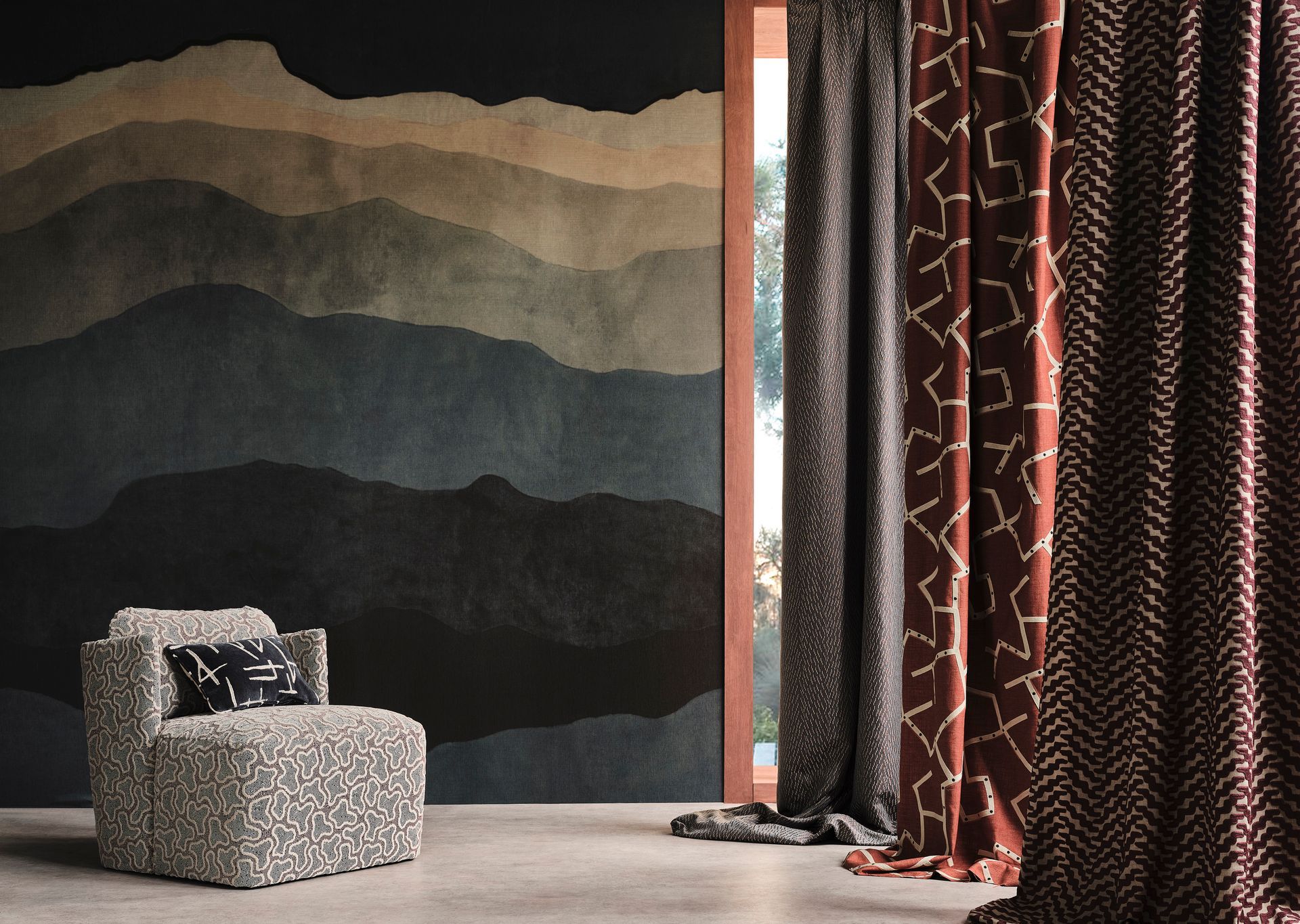Sessel vor einem Bergmotiv und gemusterten Vorhängen; erdige Farbtöne.