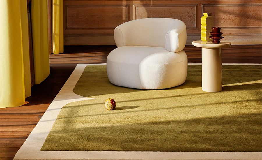 Gemütliches Interieur mit einem weißen runden Sessel, einem kleinen Tisch, einem grünen Teppich und gelben Vorhängen.