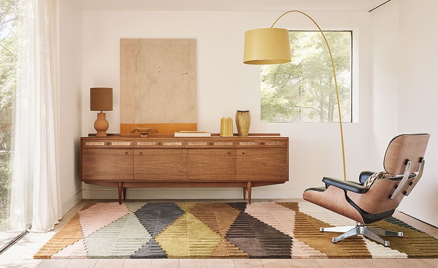 Zimmer im Mid-Century-Modern-Stil mit hölzerner Anrichte, Stehlampe und geometrischem Teppich.