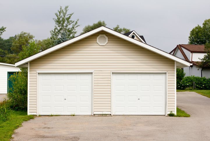 A garage with two white garage doors is next to a house.
