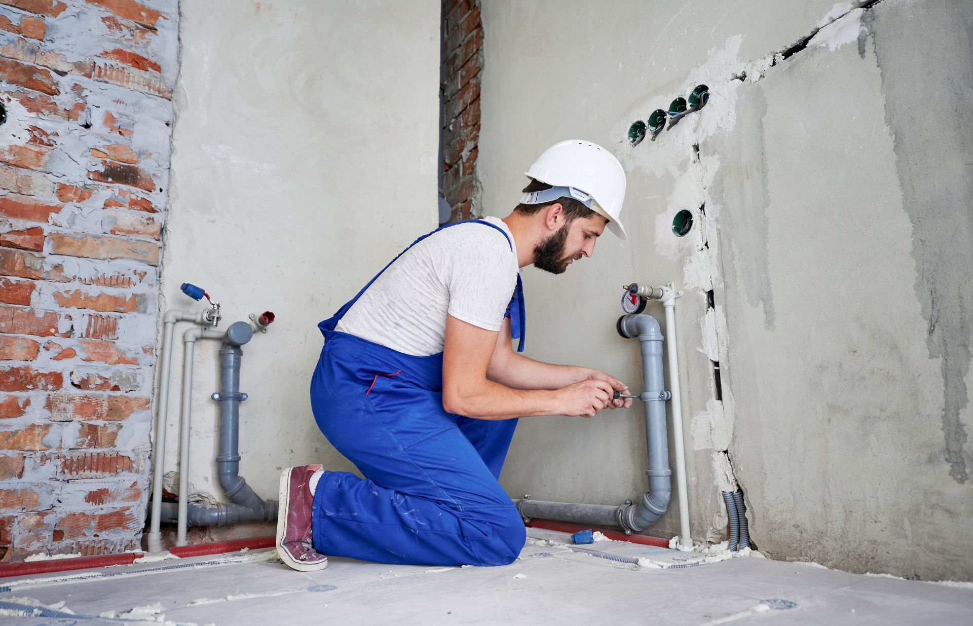 A man is kneeling down in a room fixing pipes.