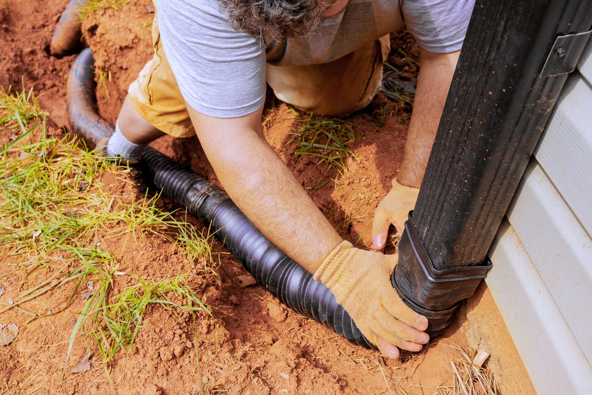 A man is kneeling down in the dirt next to a drain pipe.