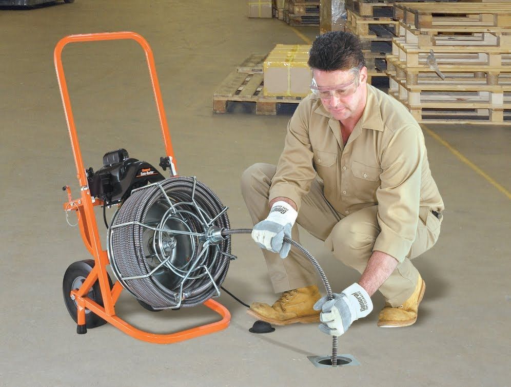 A man is kneeling down next to a drain cleaner in a warehouse.