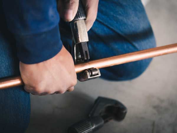 A man is cutting a copper pipe with a pipe cutter.