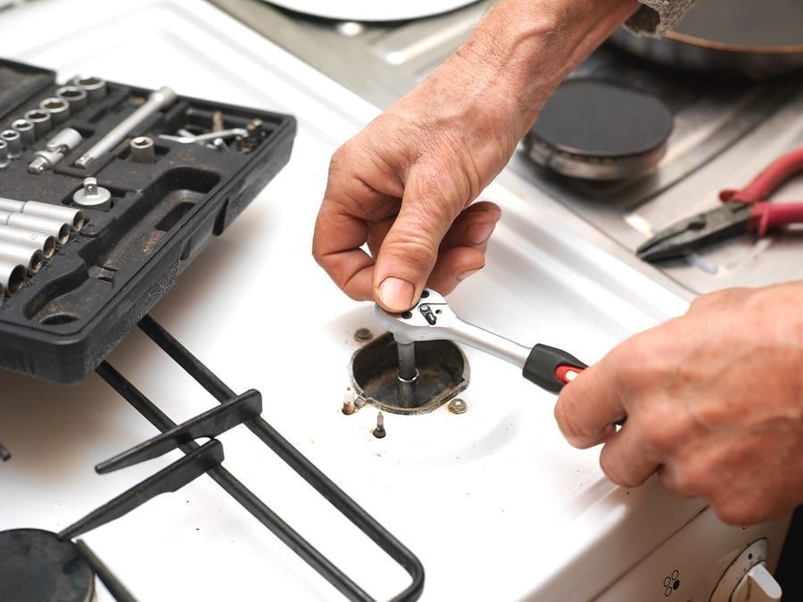 A man is fixing a gas stove with a wrench