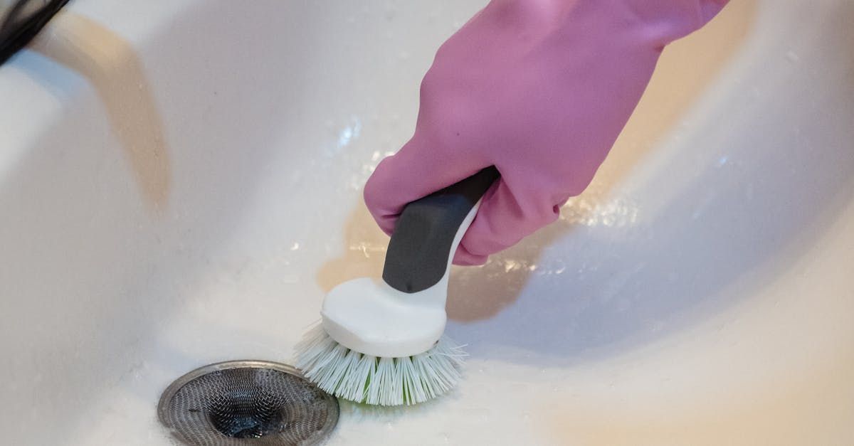 A person wearing pink gloves is cleaning a sink with a brush.