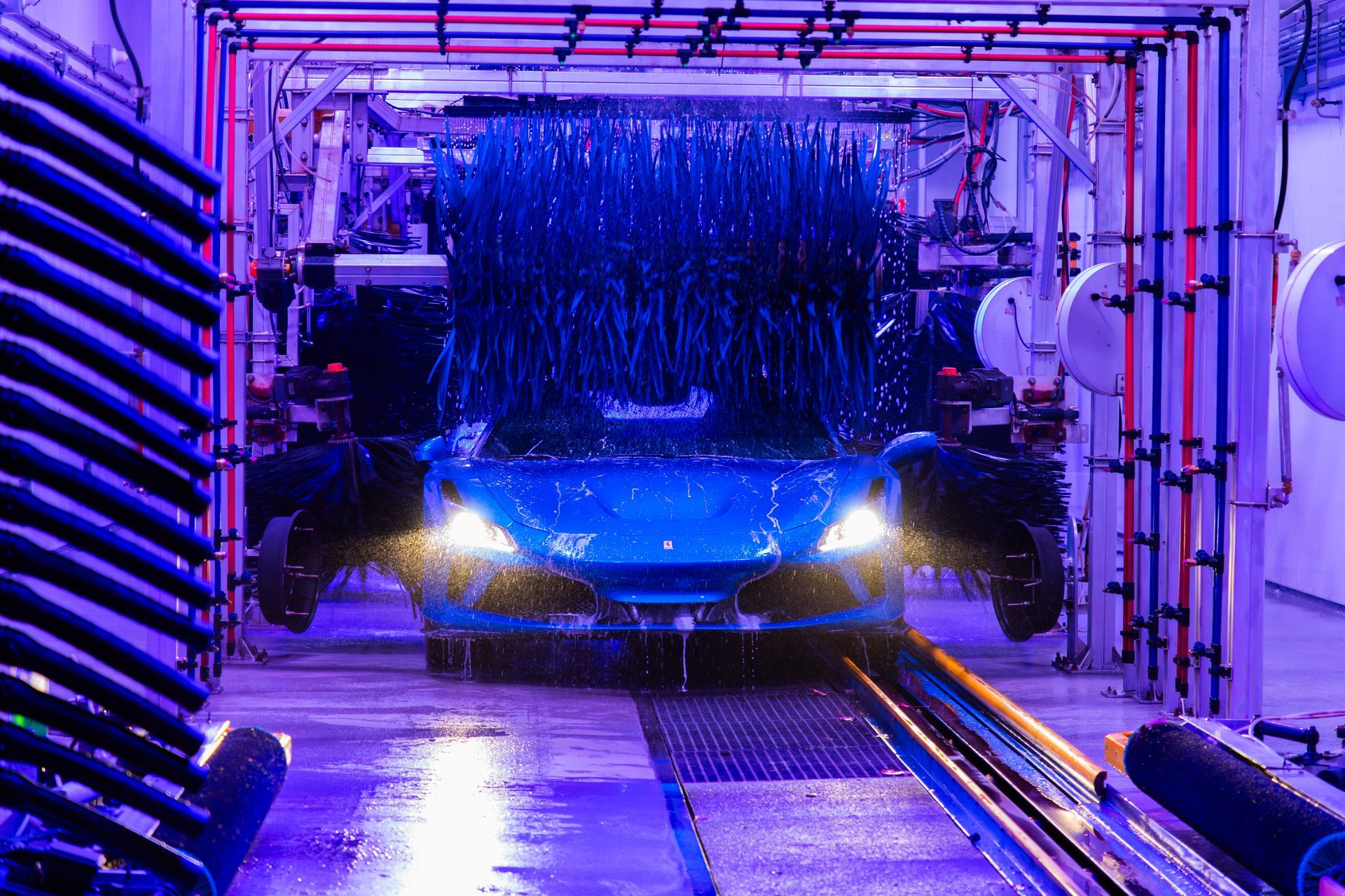 Blue car in a purple-lit automatic car wash with water spraying over the windshield