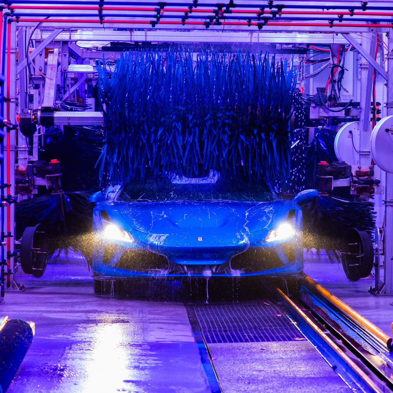 Blue car moving through a neon-lit automated car wash with brushes and water spray.
