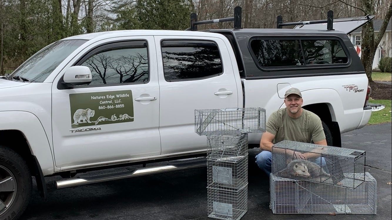 Man with traps poses by white truck; green logo on side. Outdoor setting.