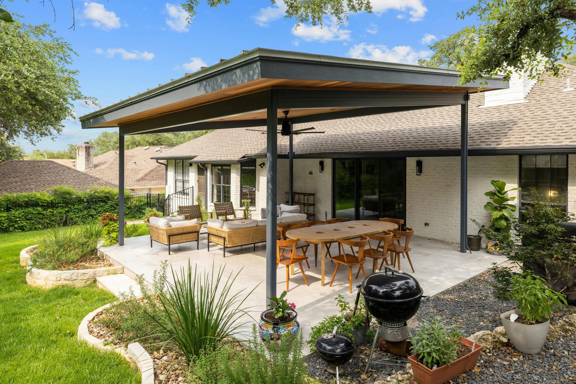 A patio with a table and chairs under a pergola in the backyard of a house.