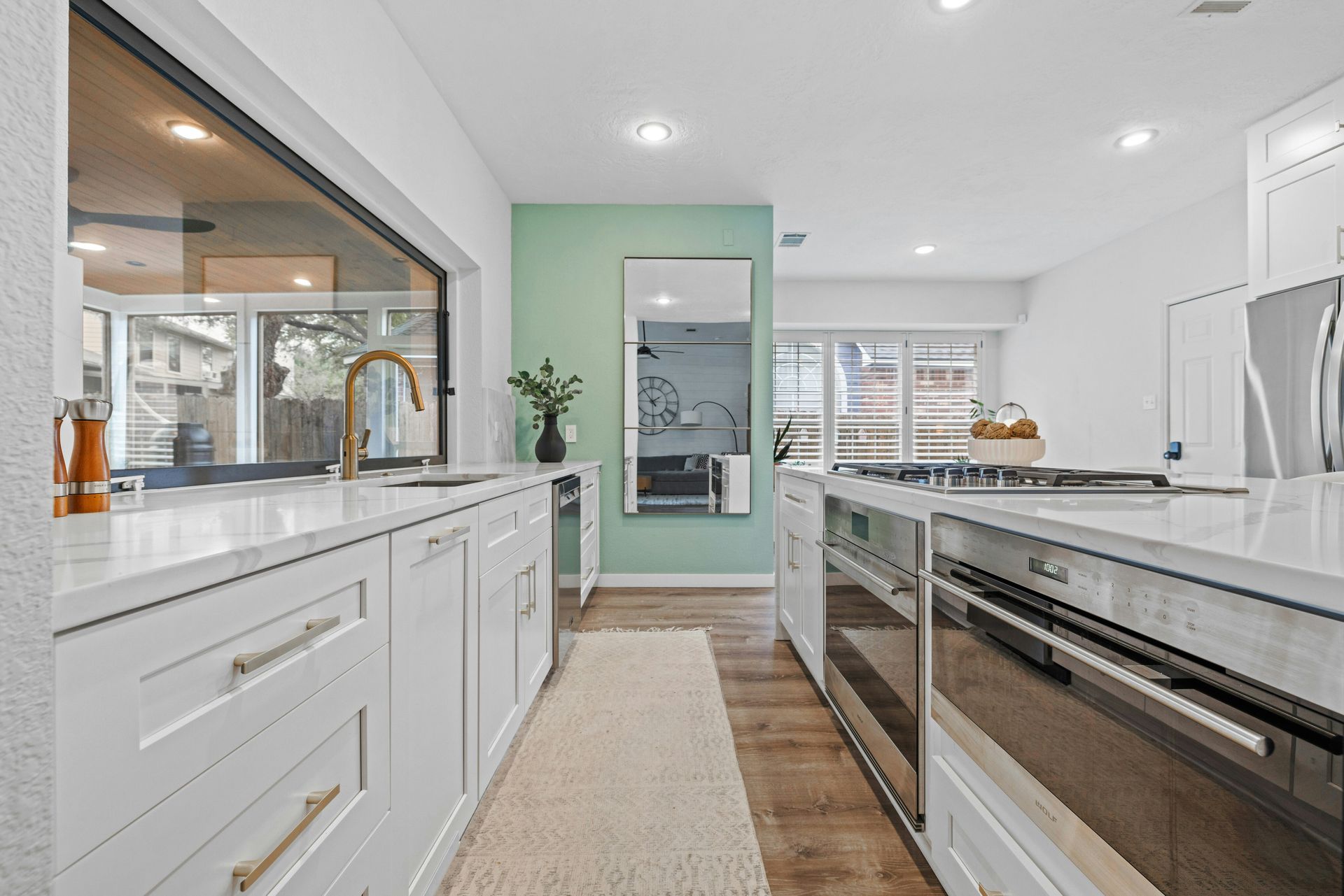 A kitchen with white cabinets and stainless steel appliances and a large mirror on the wall.