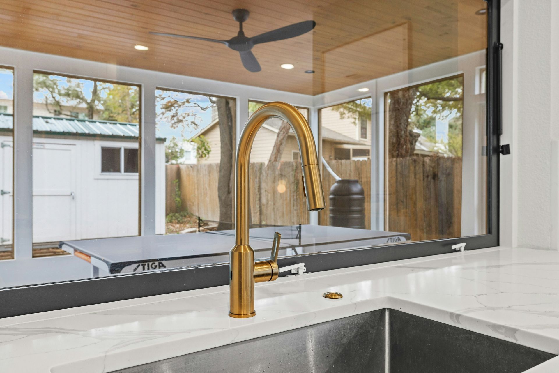 A kitchen sink with a gold faucet and a ceiling fan.