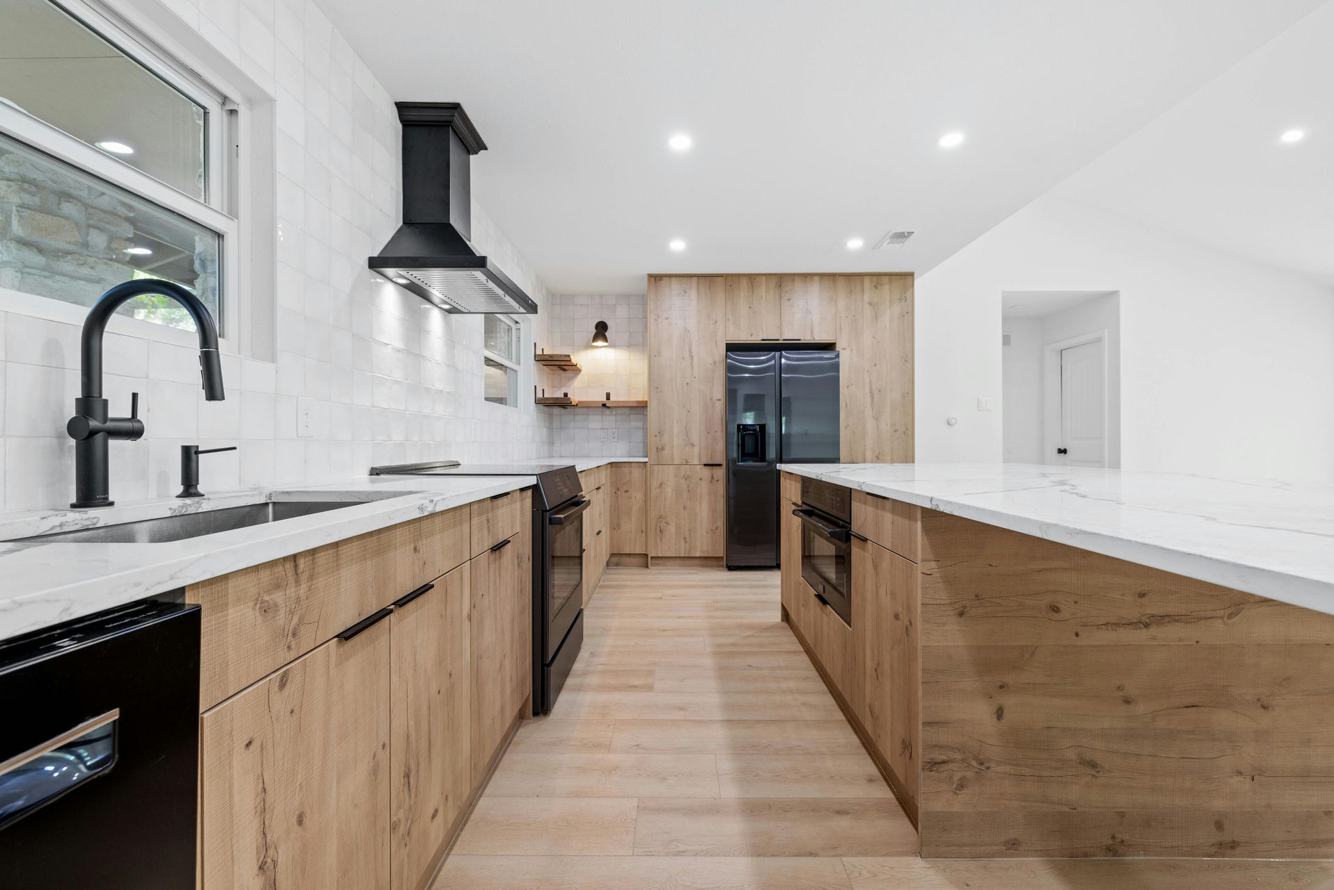 A kitchen with wooden cabinets , white counter tops , black appliances and a sink.