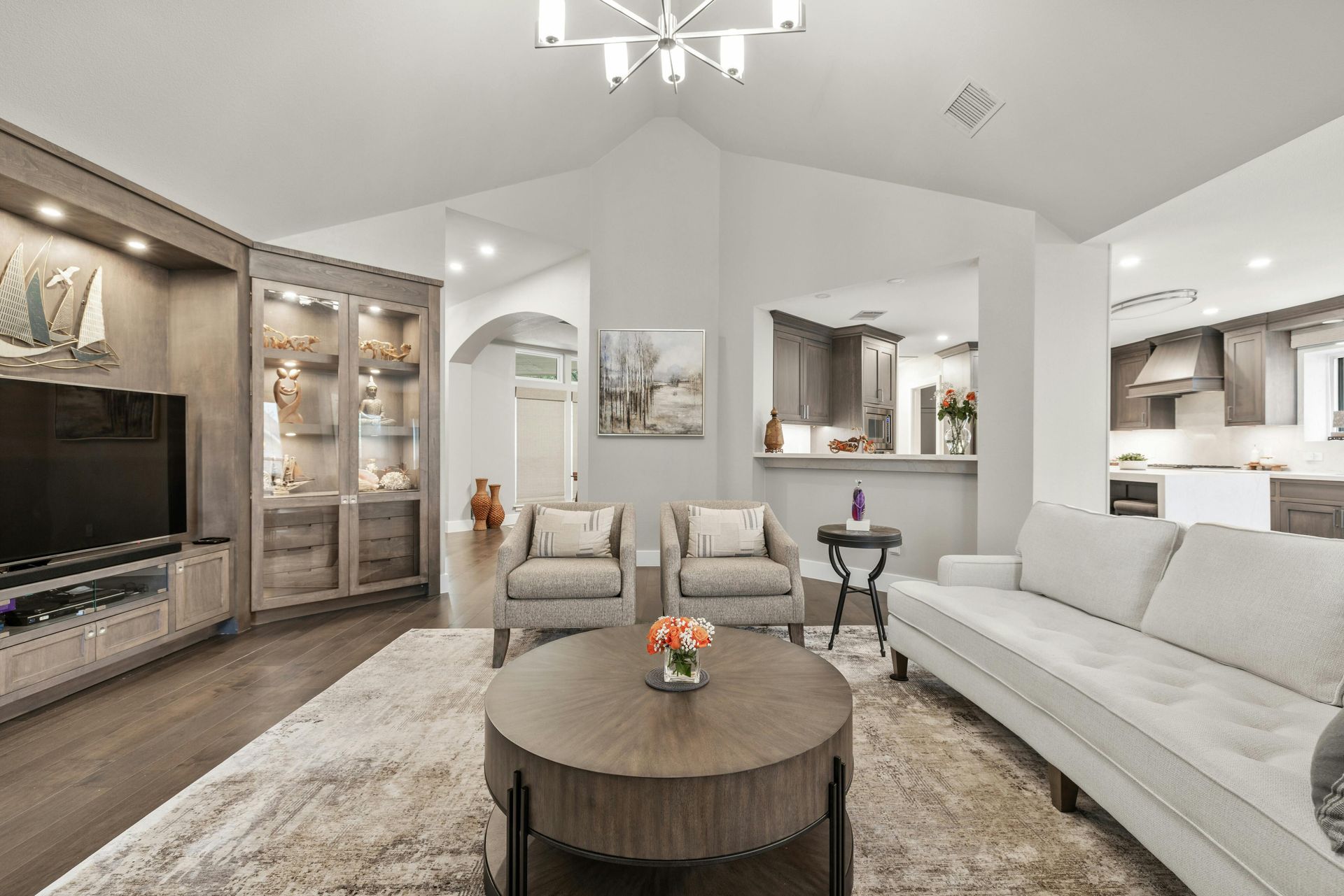 Living room with built-in cabinets, sofa, chairs, and a round coffee table; open to a kitchen.