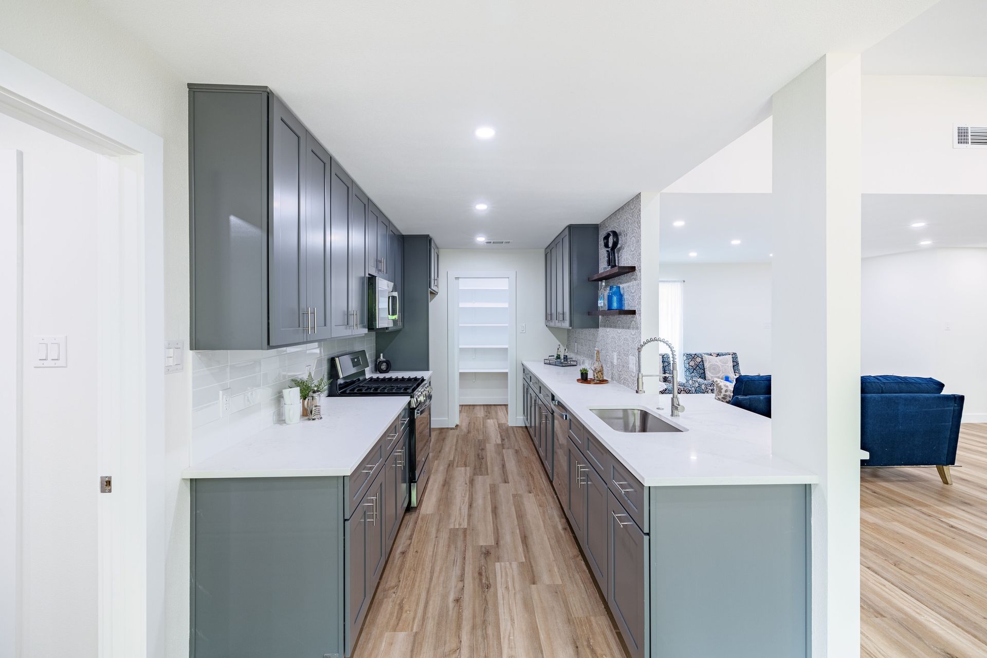A kitchen with gray cabinets , white counter tops , a sink and a stove.