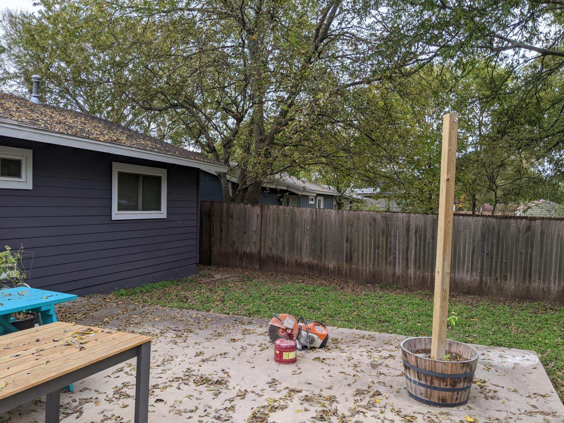 A backyard with a wooden fence , a table , and a bucket.
